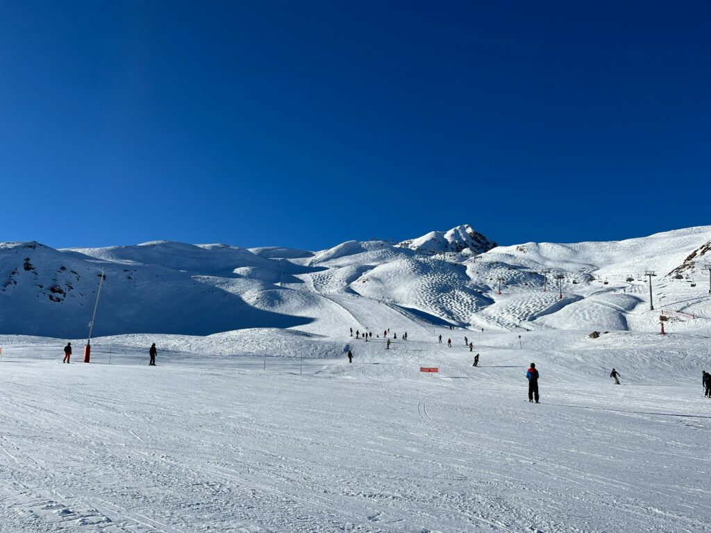 Skieurs sur les larges pistes du domaine Paradiski sous un ciel bleu